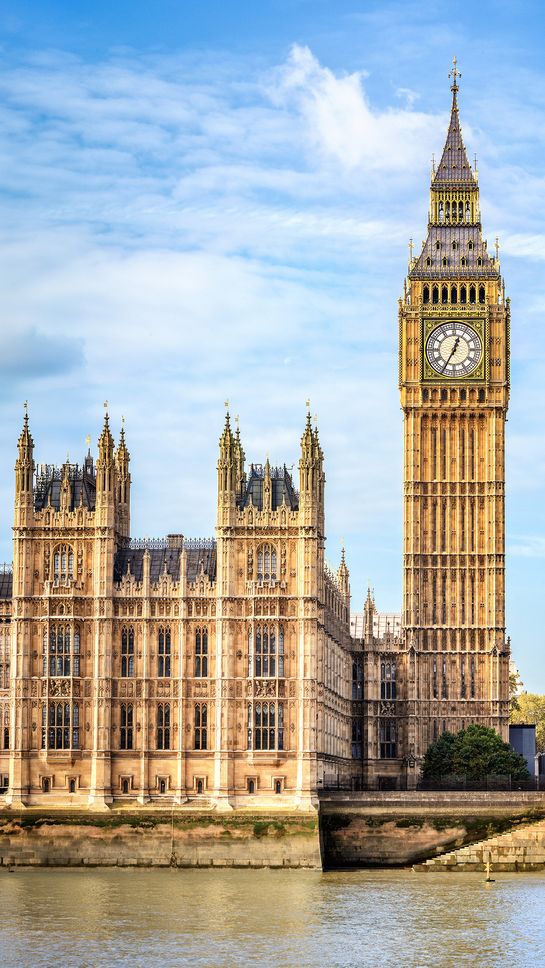 Big Ben and the Houses of Parliament in London, viewed from across the River Thames under a partly cloudy sky.