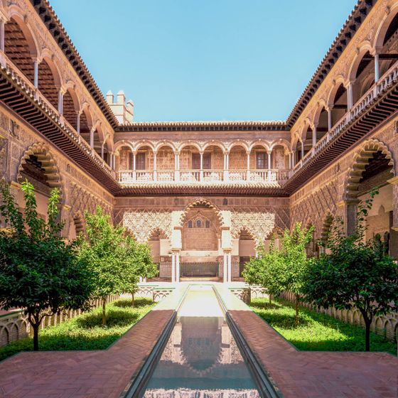 Intricate architectural courtyard with arches, central pool, and lush greenery under a clear blue sky.