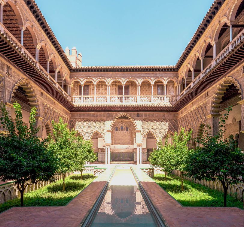 Intricate architectural courtyard with arches, central pool, and lush greenery under a clear blue sky.