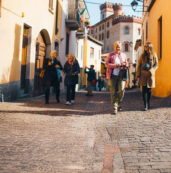 People walking on a cobblestone street in a sunny village, with a historic building in the background.