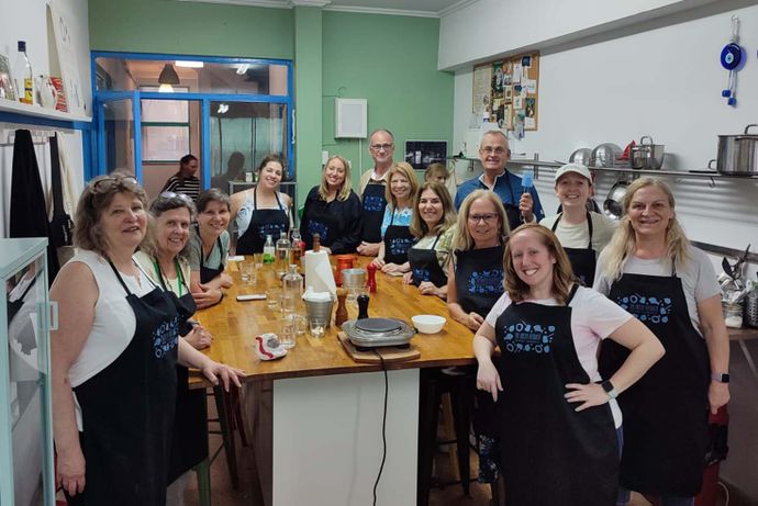 A group of people wearing aprons gather around a kitchen island in a cooking class, smiling at the camera in a well-equipped kitchen.