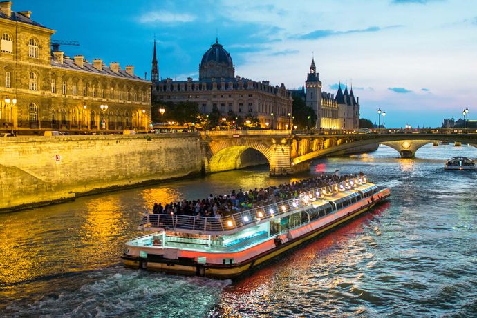 Tour boat on the Seine River at sunset, passing historic buildings and bridges in Paris, illuminated by city lights.