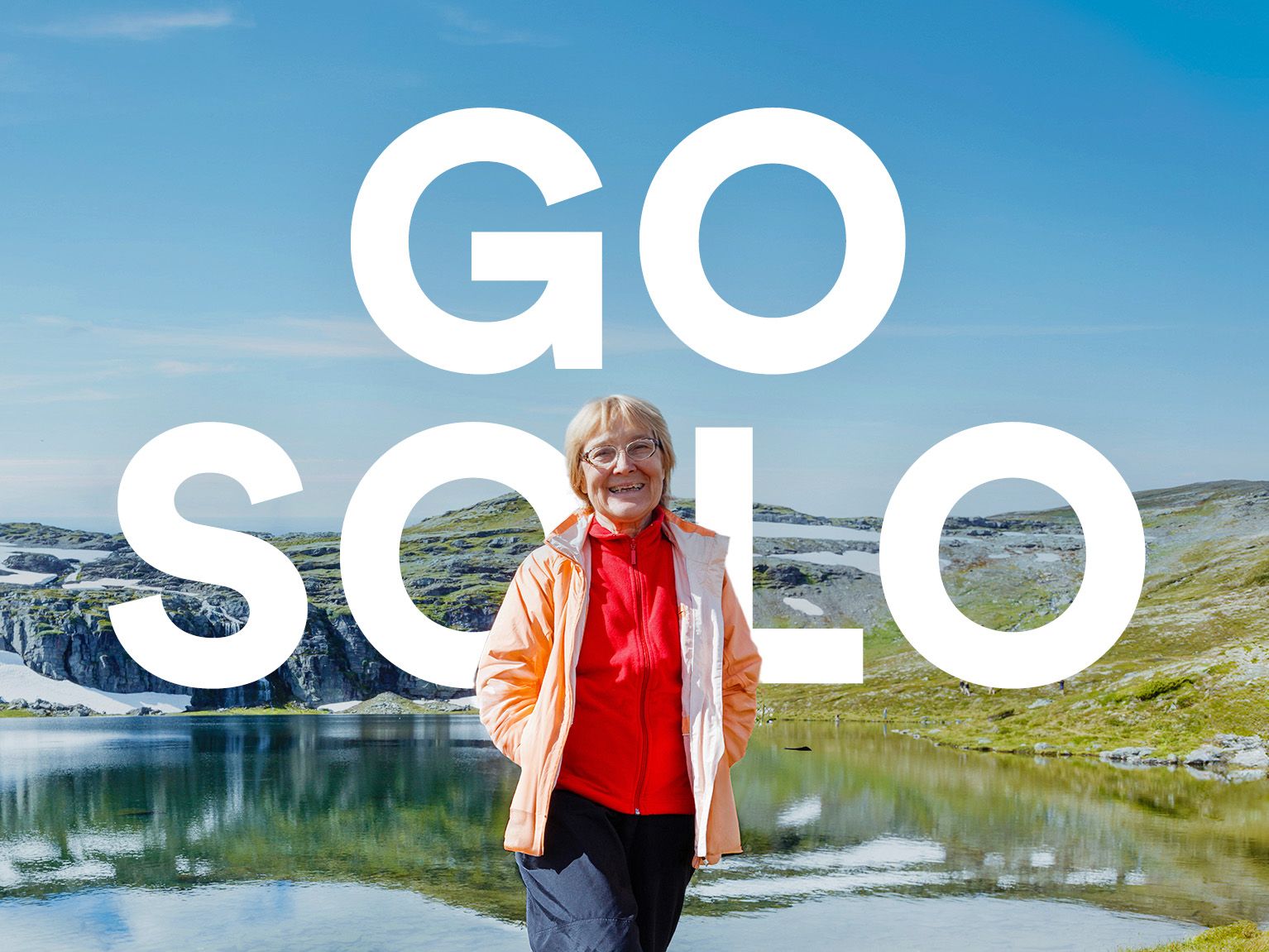 A person in outdoor gear stands by a reflective lake, green hills, and blue sky. Large text reads "GO SOLO" above.