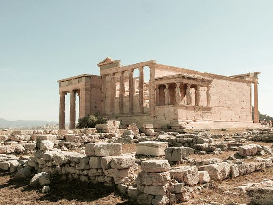 Ancient temple ruins with columns and statues, surrounded by scattered stones under a clear sky.