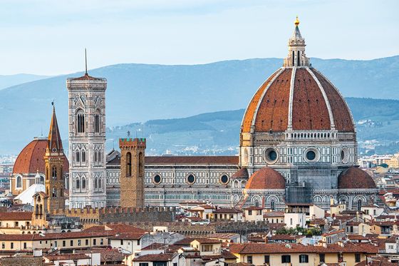 Aerial view of Florence featuring the Florence Cathedral with its iconic red dome and bell tower, set against a backdrop of distant hills.