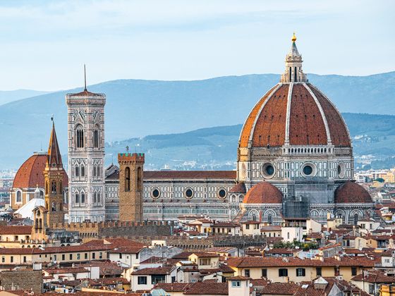 Aerial view of Florence featuring the Florence Cathedral with its iconic red dome and bell tower, set against a backdrop of distant hills.