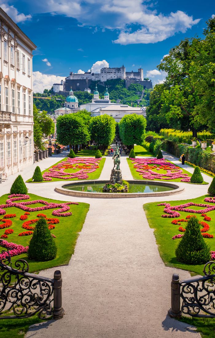 Mirabell Gardens in Salzburg, Austria, showcasing vibrant flowerbeds, statues, and Hohensalzburg Fortress in the background under a blue sky.