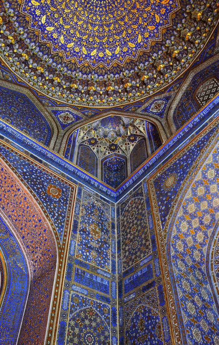 Intricate blue and gold mosaic patterns adorn the interior of a dome with ornate arches, showcasing Islamic architectural artistry.