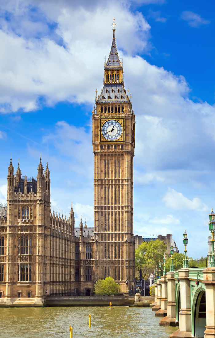 Big Ben clock tower in London against a blue sky with clouds, adjacent to the River Thames and Westminster Bridge.