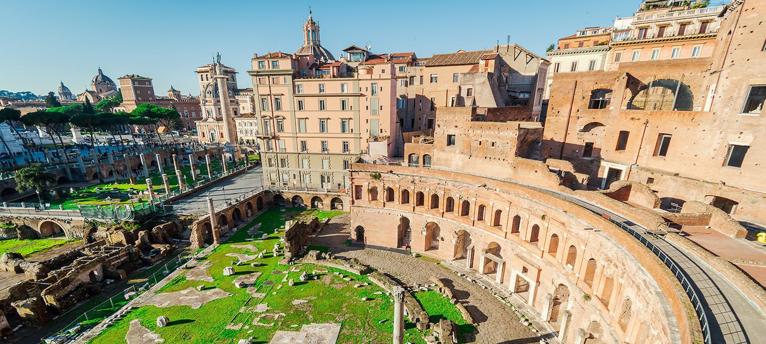 Aerial view of Trajan's Market in Rome, showcasing ancient ruins, arched structures, and surrounding historic buildings under a clear blue sky.