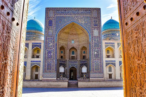 Ornate entrance view of a majestic mosque with blue domes, intricate tilework, and grand archways in a clear sky setting.