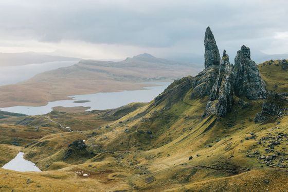 Scenic view of Old Man of Storr, featuring rugged rock formations and rolling hills under a cloudy sky on the Isle of Skye, Scotland.