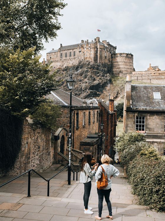 Two people standing on a cobblestone street with Edinburgh Castle in the background on a cloudy day.