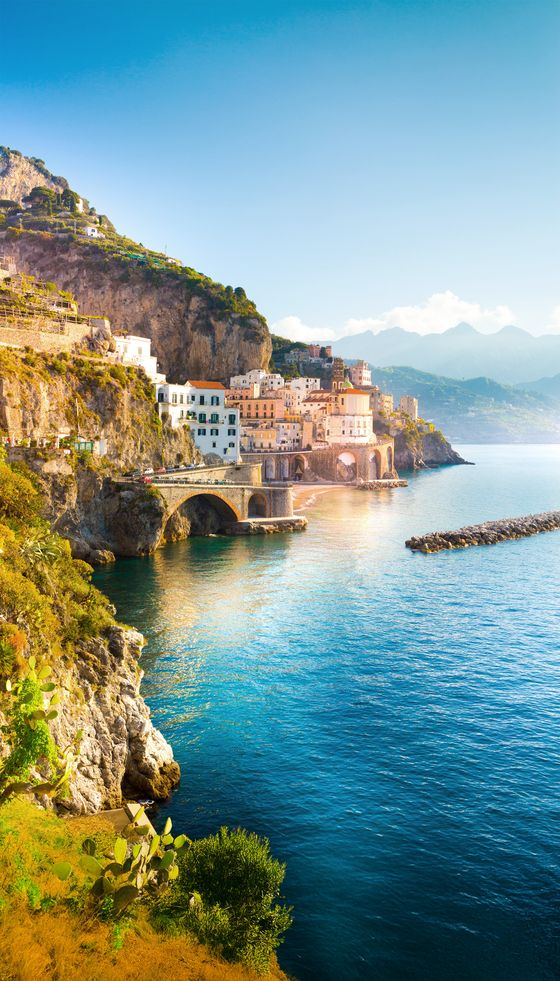 Cliffside village with colorful buildings over clear blue sea, set against a mountain backdrop under a bright, clear sky.