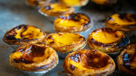 Close-up of freshly baked egg tarts with golden, flaky crusts and caramelized tops, arranged on a baking tray.