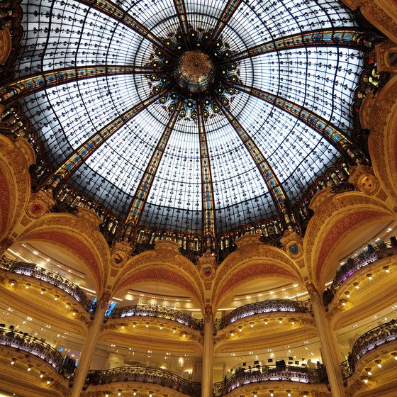 Ornate glass dome ceiling with intricate patterns, overlooking multiple floors of a grand, elegantly decorated interior space.