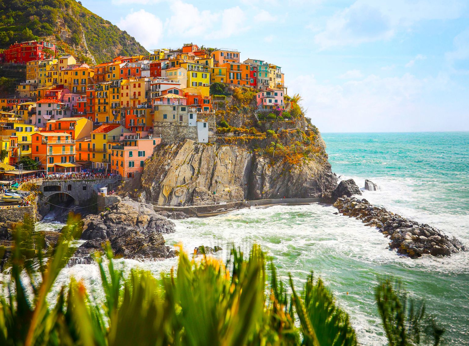 Colorful cliffside village overlooking the ocean, with vibrant buildings and lush greenery under a bright blue sky.