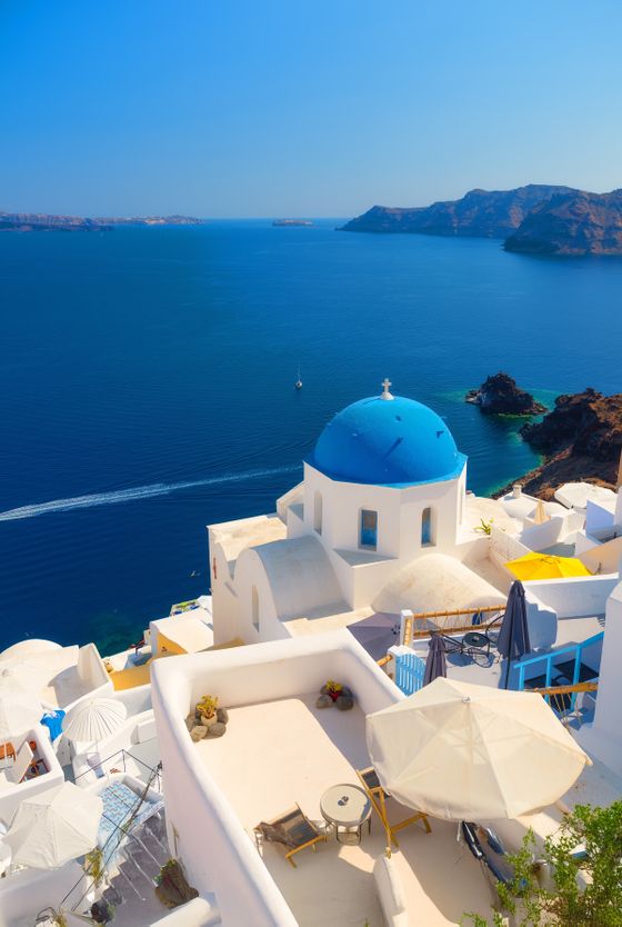 White buildings with blue dome roofs overlook the Aegean Sea in Santorini, Greece, under a clear blue sky.