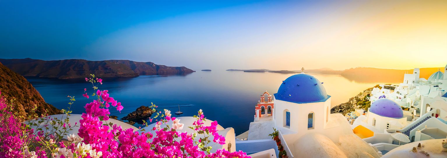 Panoramic view of Santorini at sunset, featuring a blue-domed church, pink flowers, and a tranquil sea against a colorful sky.