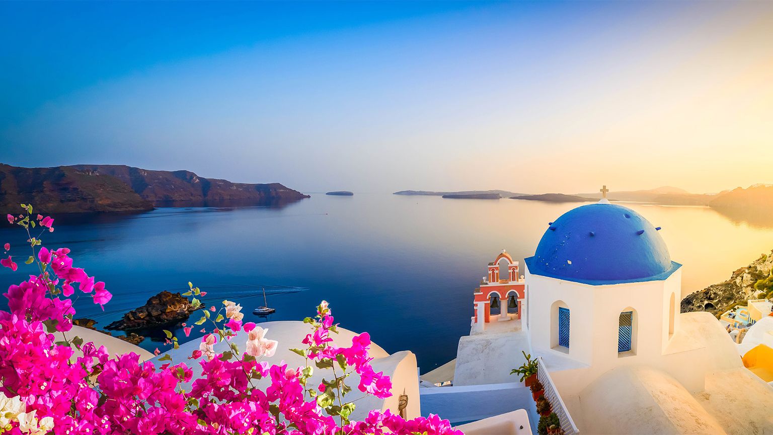 Panoramic view of Santorini at sunset, featuring a blue-domed church, pink flowers, and a tranquil sea against a colorful sky.