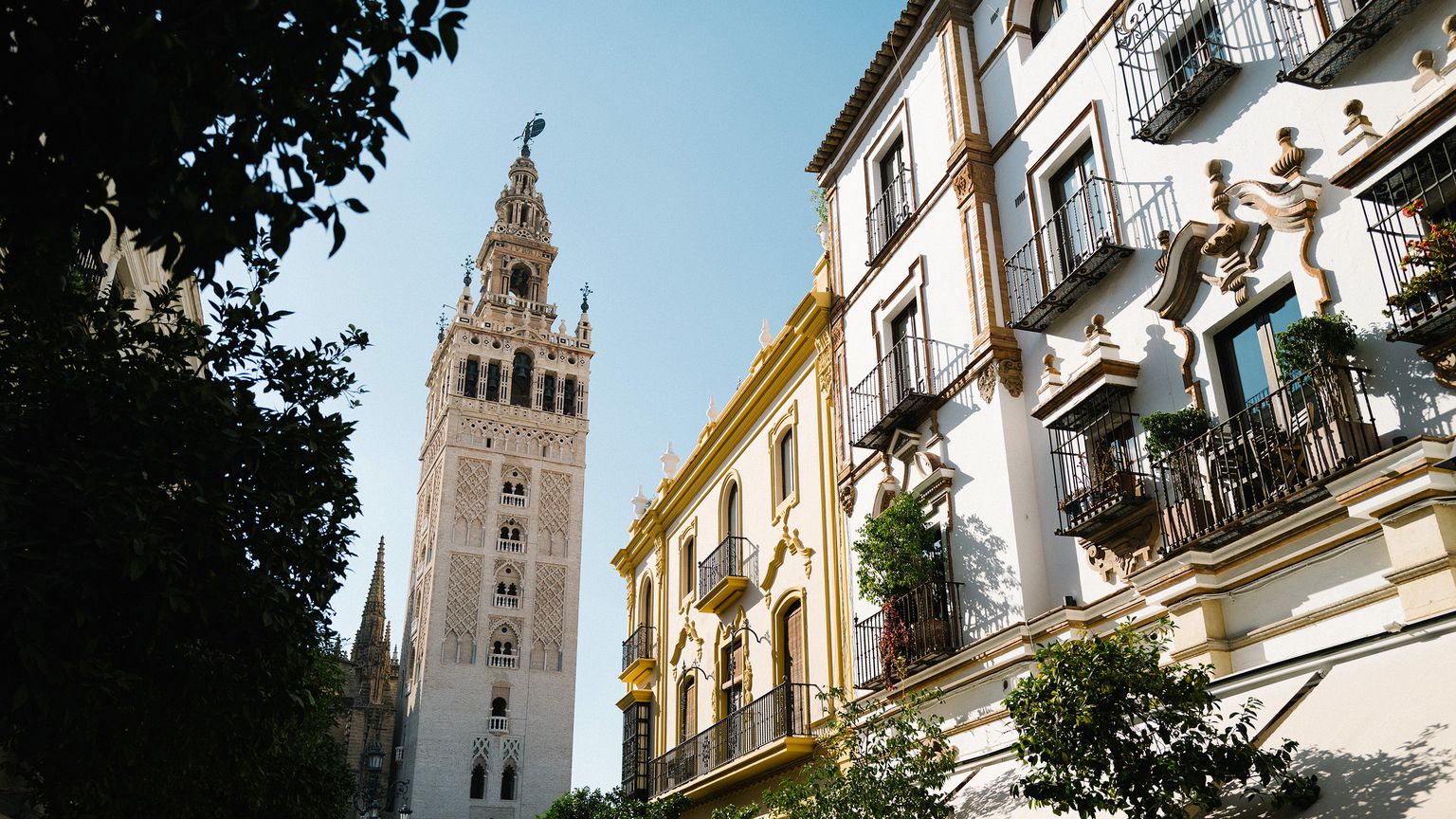 Giralda tower and ornate buildings in Seville, with wrought iron balconies and greenery, under a clear blue sky.