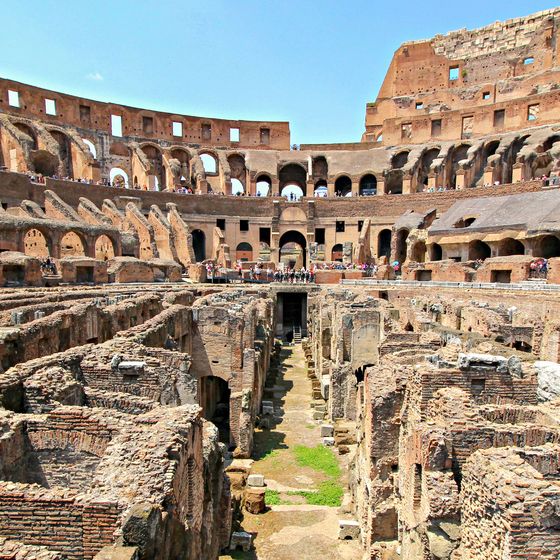 Interior view of the Roman Colosseum, showcasing ancient arches and structural details, with scattered visitors exploring the ruins.