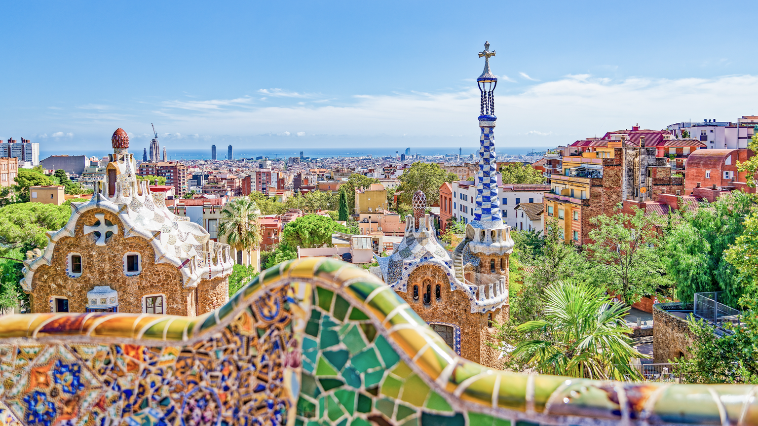 View of Barcelona from Park Güell, featuring colorful mosaics, unique architecture, and a cityscape with the sea on the horizon.