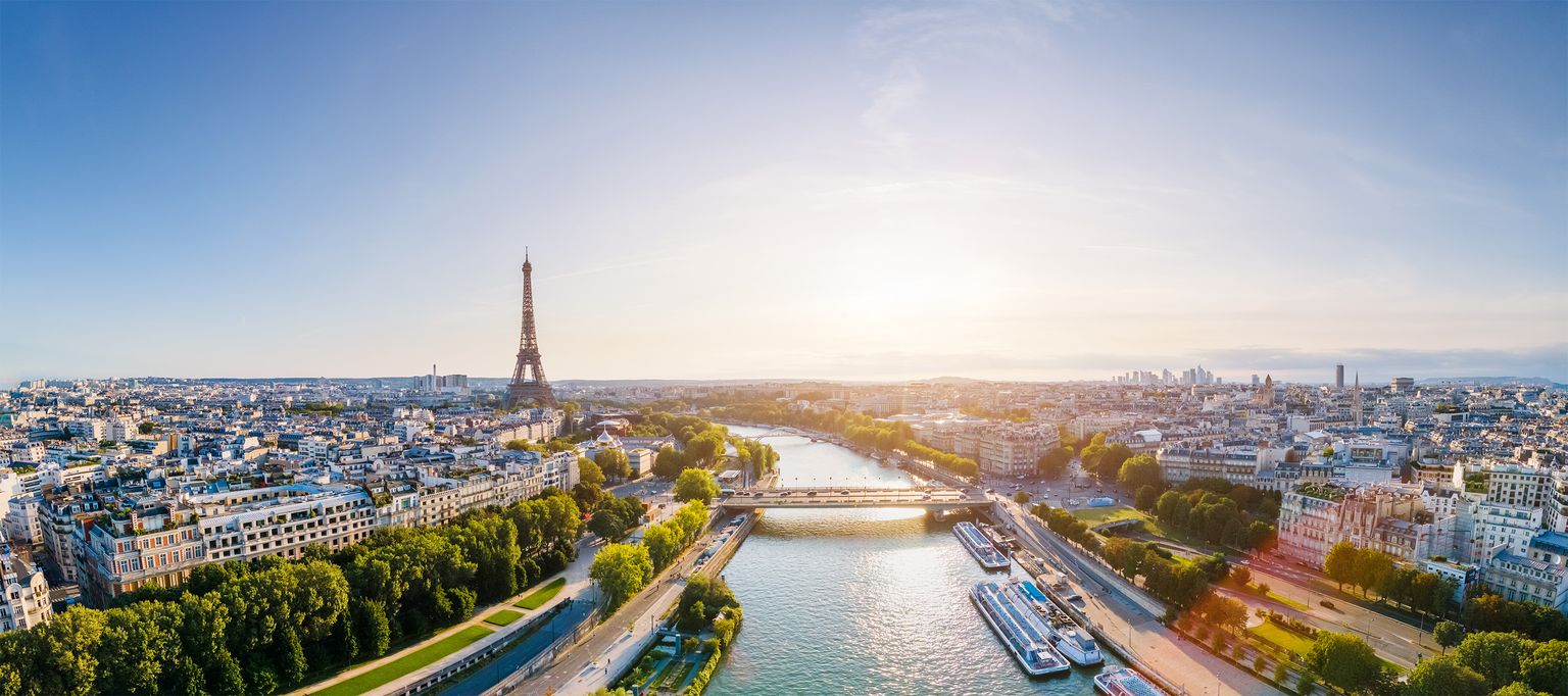 Panoramic view of Paris with the Eiffel Tower, Seine River, and cityscape under a clear blue sky at sunset.