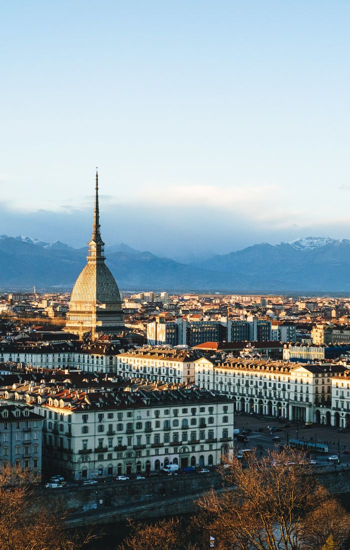 Panoramic view of Turin, Italy, with the domed Mole Antonelliana rising above the city and snow-capped mountains in the distance.