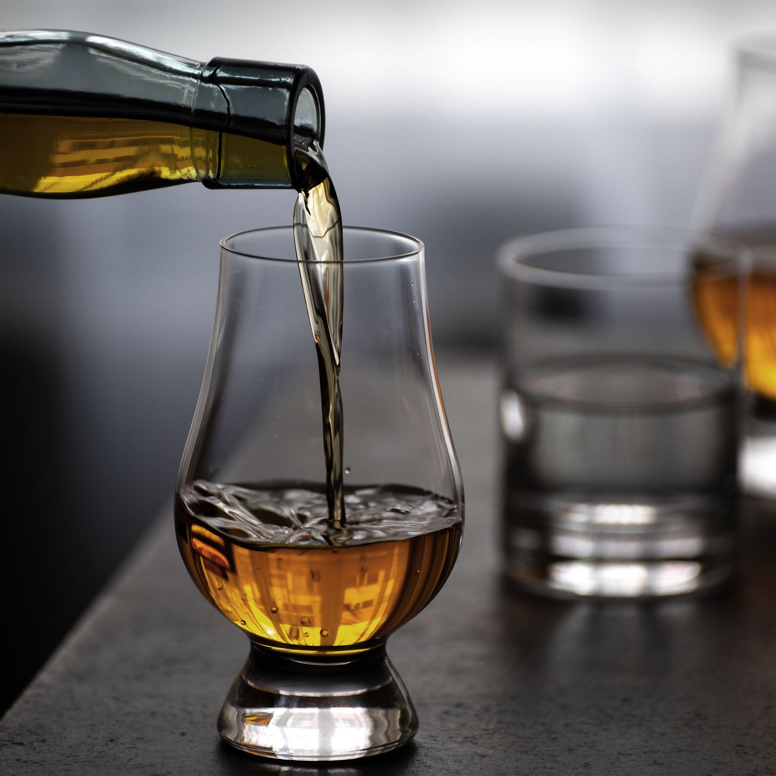 Pouring whiskey into a glass on a table with two other filled glasses, creating a warm and inviting atmosphere.