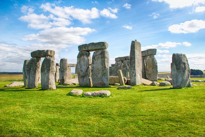 Stonehenge with blue sky and scattered clouds, featuring large standing stones on a grassy field.