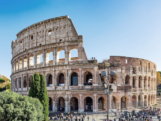 The Colosseum in Rome, Italy, partially intact, with a blue sky and people walking around its base.