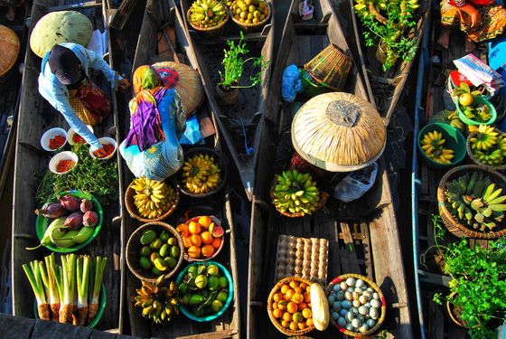 Aerial view of a vibrant floating market with boats filled with fruits, vegetables, and spices, as vendors sell their goods.