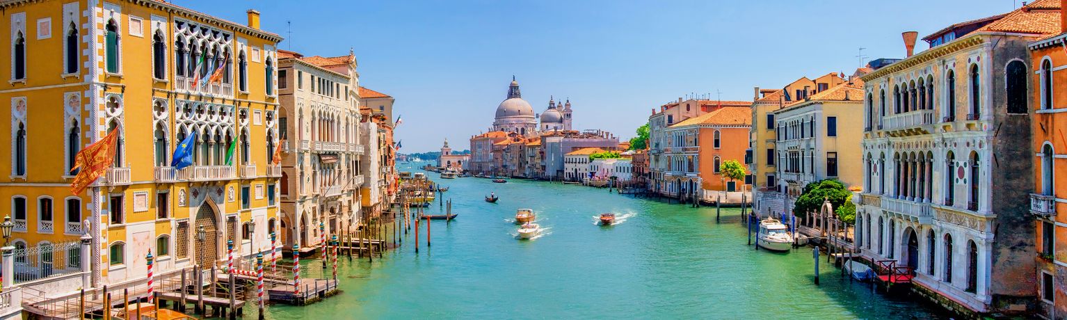 Scenic view of a Venice canal with colorful historic buildings, boats on the turquoise water, and a domed church in the background.