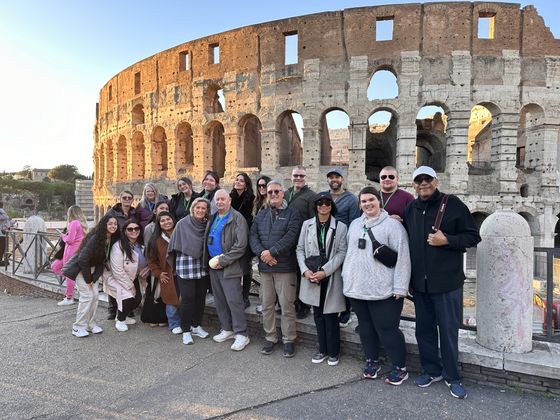 A group of people posing in front of the Colosseum in Rome, Italy, during the day.