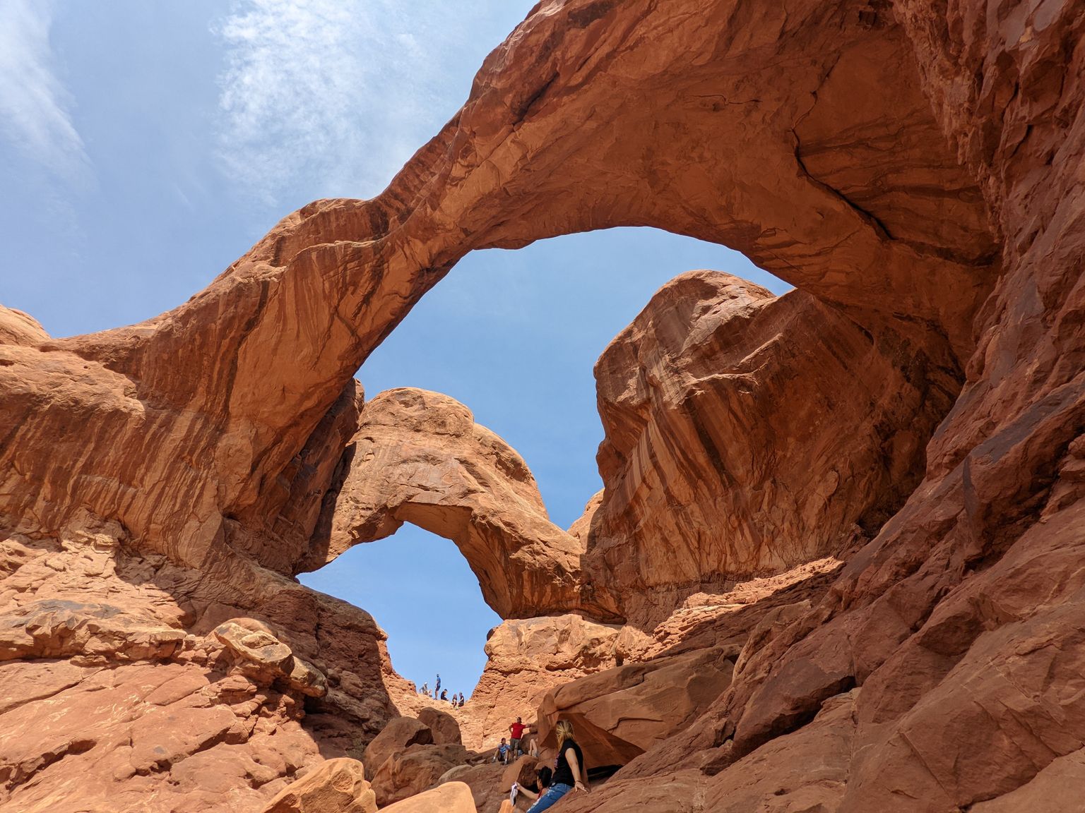 Red sandstone arches with people beneath, set against a clear blue sky, showcasing natural rock formations and textures.