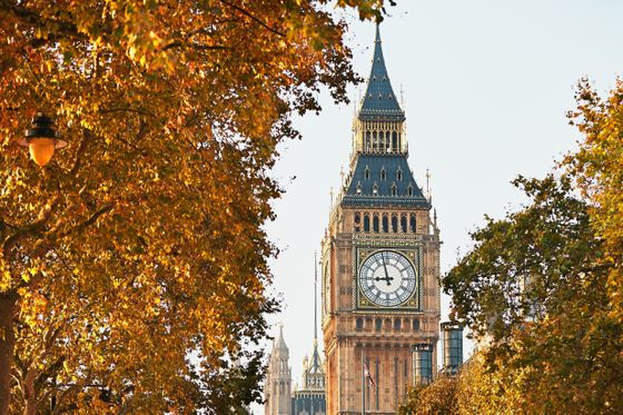 Big Ben framed by autumn leaves, with a clear blue sky in the background.