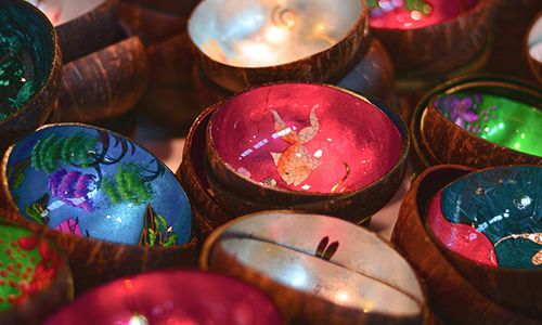 Colorful lacquered coconut shell bowls with intricate paintings and shiny interiors, including a mermaid and underwater scenes, are displayed.