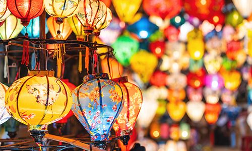 Colorful decorative lanterns with intricate patterns hang in a vibrant market, creating a lively and festive atmosphere.