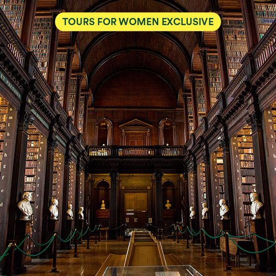 A grand, ornate library hall with tall bookshelves, statues, and arched ceilings, featuring a "Tours for Women Exclusive" sign above.