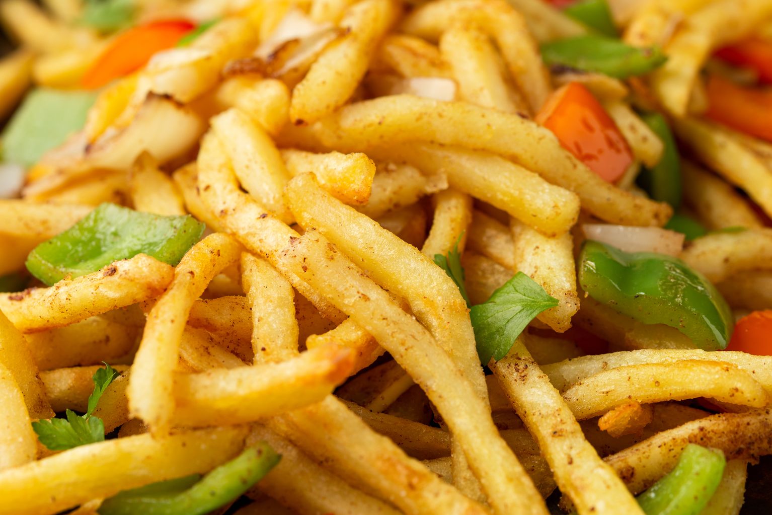 A close-up of seasoned french fries mixed with chunks of green bell pepper, red bell pepper, white onion, and fresh parsley leaves.