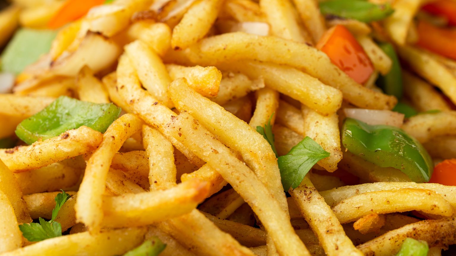 A close-up of seasoned french fries mixed with chunks of green bell pepper, red bell pepper, white onion, and fresh parsley leaves.
