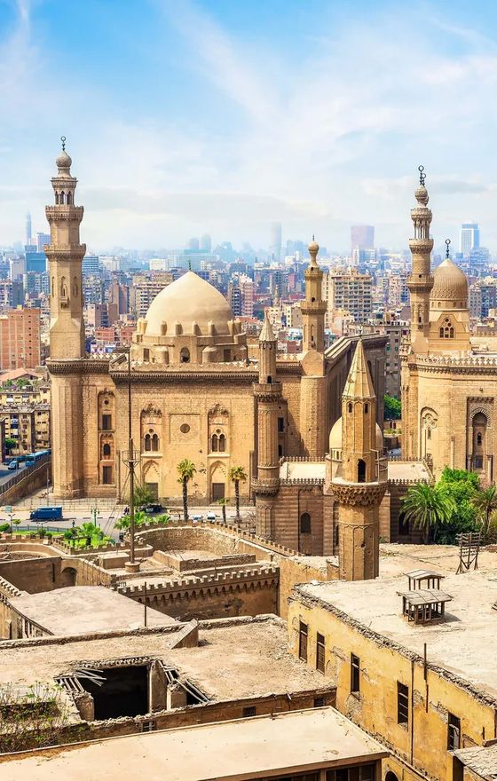 Historic mosque with domes and minarets in Cairo, Egypt, set against a cityscape under a clear blue sky.
