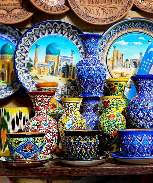 Colorful handcrafted pottery with intricate patterns, including plates, vases, and cups, displayed on a shelf.