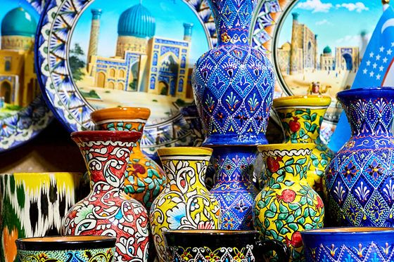 Colorful handcrafted pottery with intricate patterns, including plates, vases, and cups, displayed on a shelf.