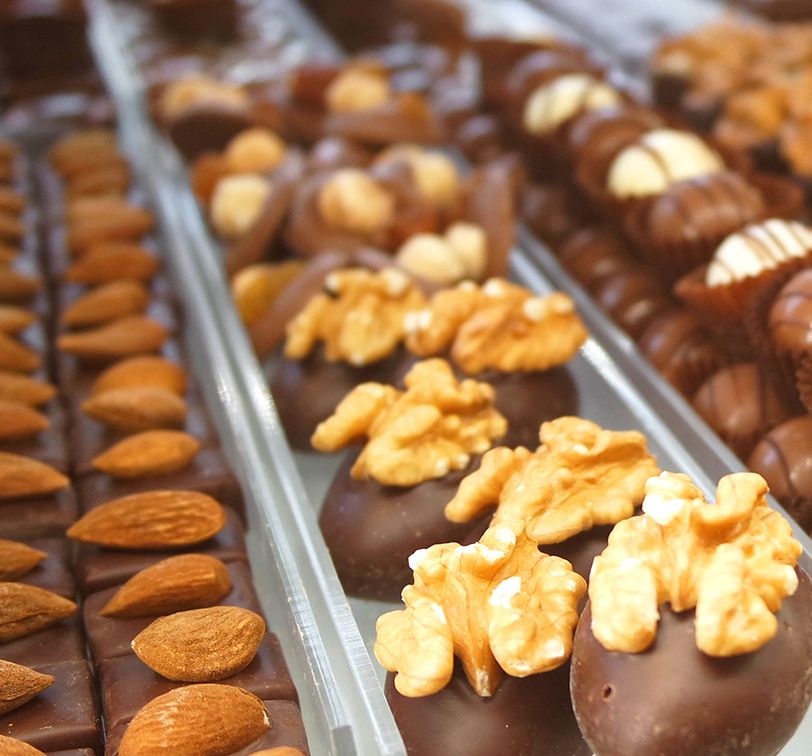 Assorted chocolates topped with almonds and walnuts, displayed in rows on a counter.