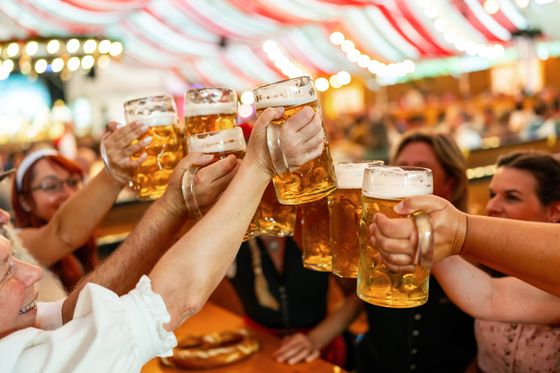 People clinking large beer mugs at a festive gathering with red and white tent decor in the background.