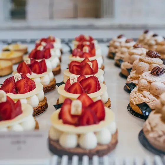 Rows of elegant pastries topped with fresh strawberries and cream, displayed on a counter with a blurred background.