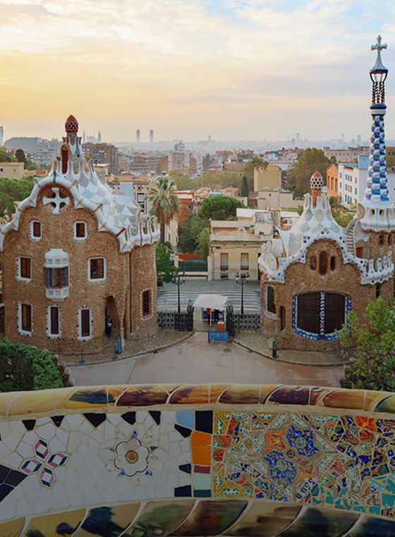 Park Güell in Barcelona at sunset, showcasing colorful mosaic benches and whimsical architecture with cityscape in the background.