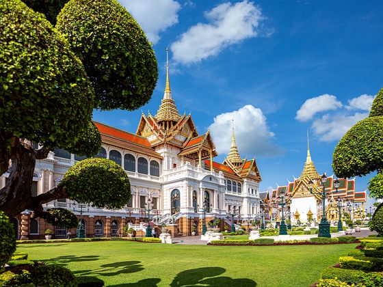 Ornate palace with golden spires and lush gardens under a bright blue sky with scattered clouds.